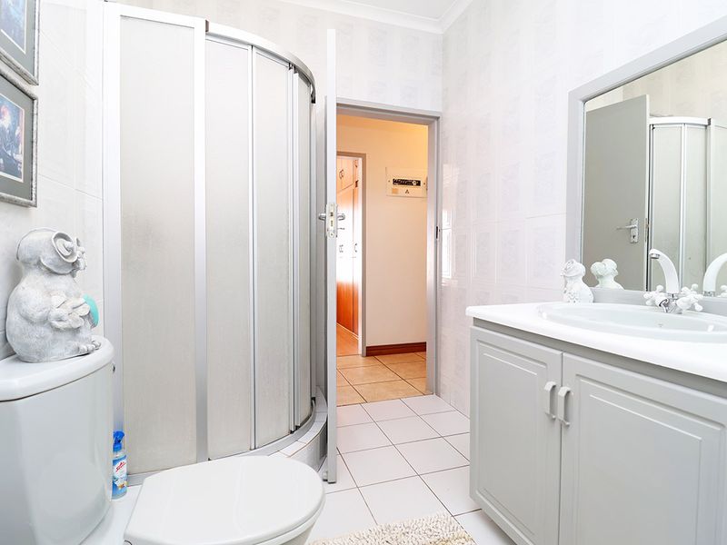 A functional bathroom featuring a curved shower enclosure, a vanity cabinet with an integrated basin, and neutral tiled finishes.