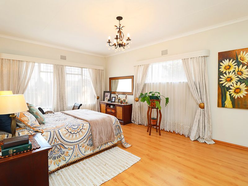 A spacious, well-lit bedroom featuring laminate flooring, large windows with curtain treatments, and a central ceiling light fixture.