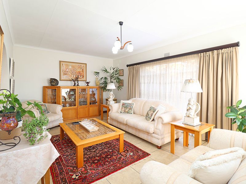 A well-maintained living room featuring neutral tiled flooring, large windows with curtain treatments, and a central ceiling light fixture.