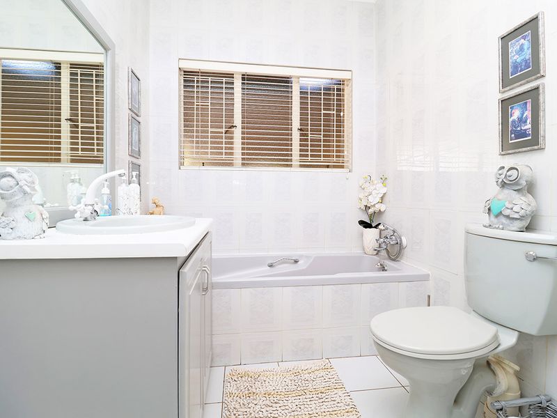 A functional bathroom featuring a built-in vanity with basin, a bathtub, and a toilet, finished with neutral wall and floor tiling.