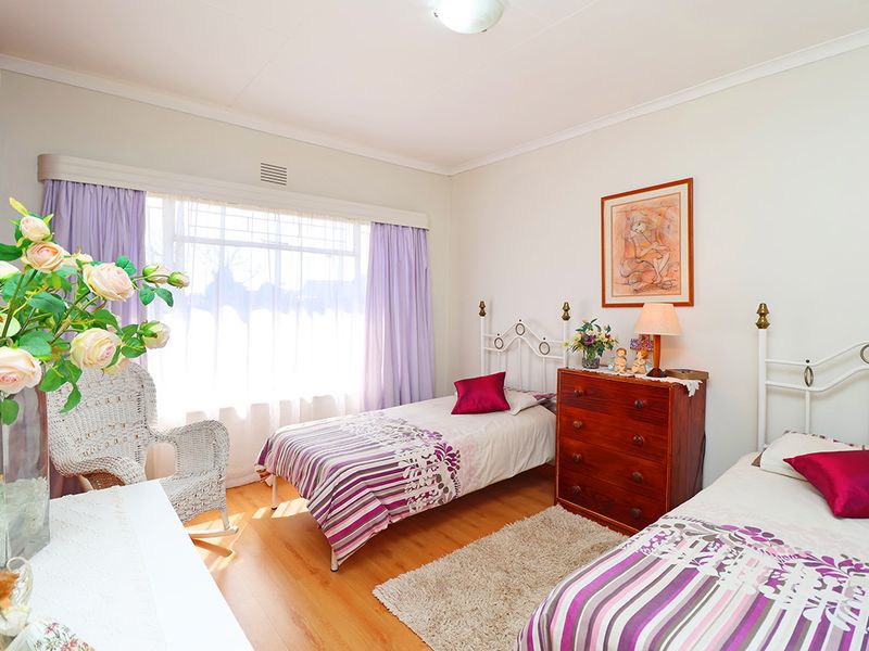 A well-lit bedroom featuring laminate flooring, built-in cupboards, and a large window allowing for ample natural light.