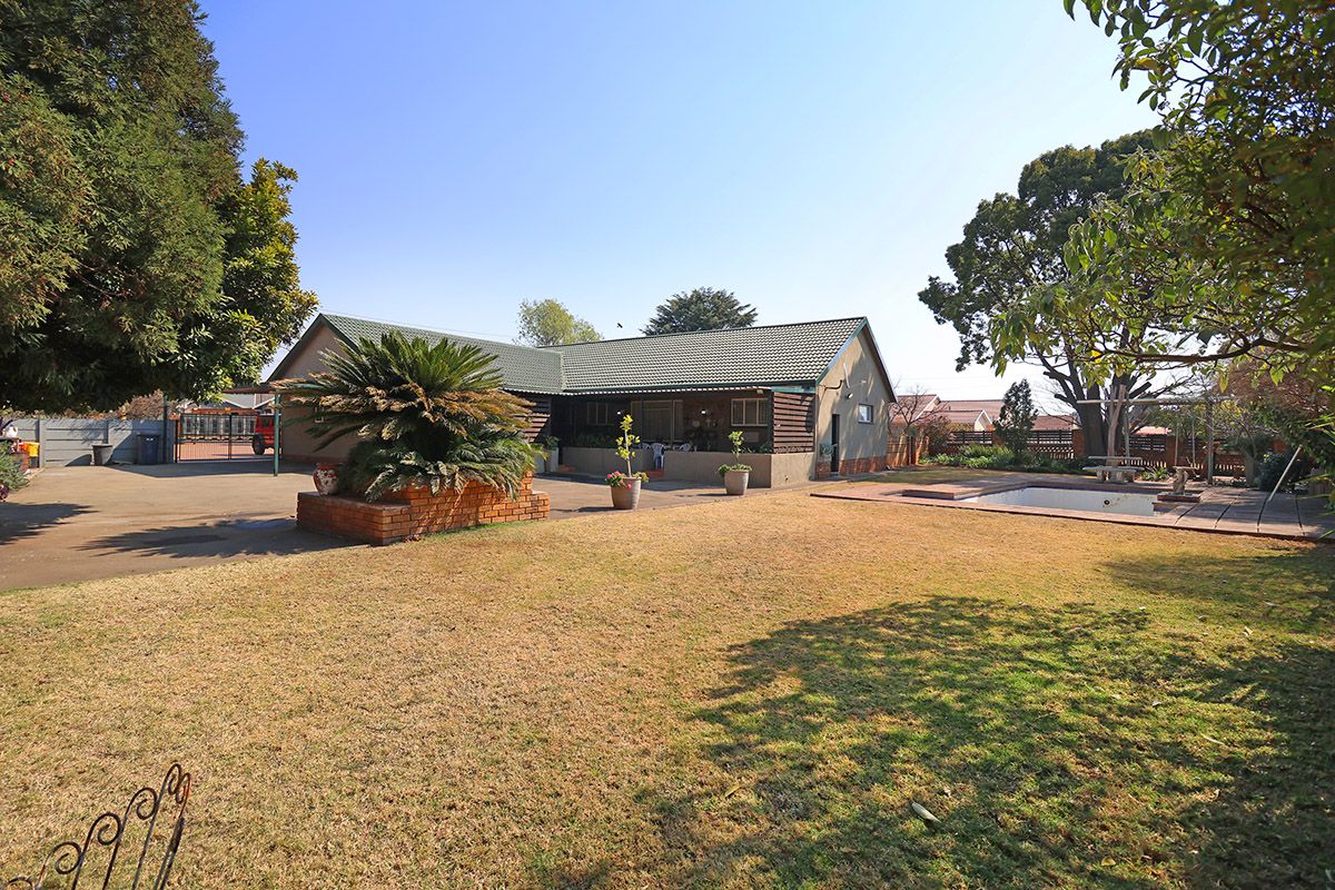 Rear view of the property featuring a swimming pool, paved patio area, and a spacious garden with established trees.