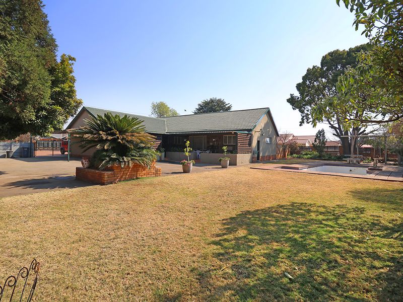 Rear view of the property featuring a swimming pool, paved patio area, and a spacious garden with established trees.