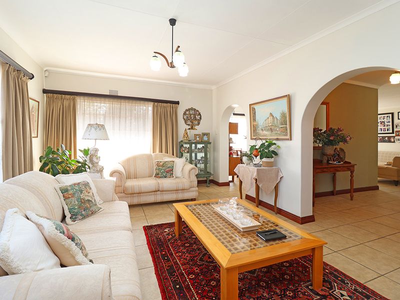 A spacious living room featuring tiled flooring, coved ceilings, and an open-plan archway leading to an adjacent area.