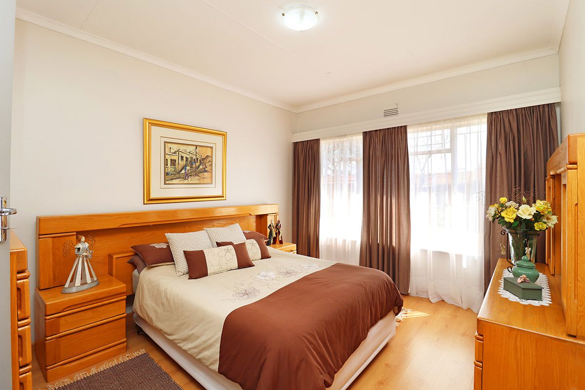 A well-maintained bedroom featuring laminate flooring, cove cornicing, and a large window allowing natural light, providing a comfortable and functional living space.