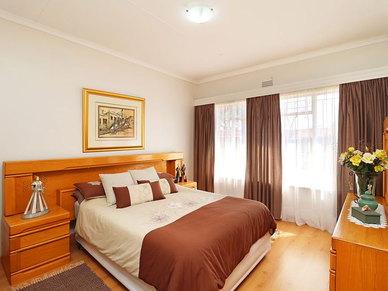 A well-maintained bedroom featuring laminate flooring, cove cornicing, and a large window allowing natural light, providing a comfortable and functional living space.