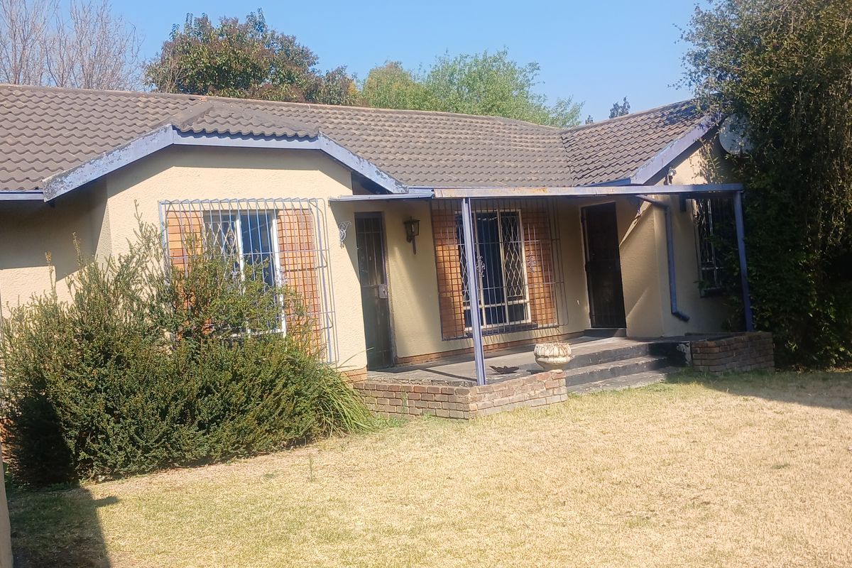 Rear view of a single-story house featuring a covered patio, security bars on windows, and a tiled roof with visible exterior maintenance requirements.