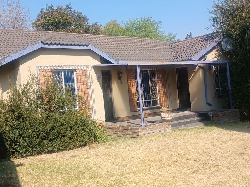Rear view of a single-story house featuring a covered patio, security bars on windows, and a tiled roof with visible exterior maintenance requirements.