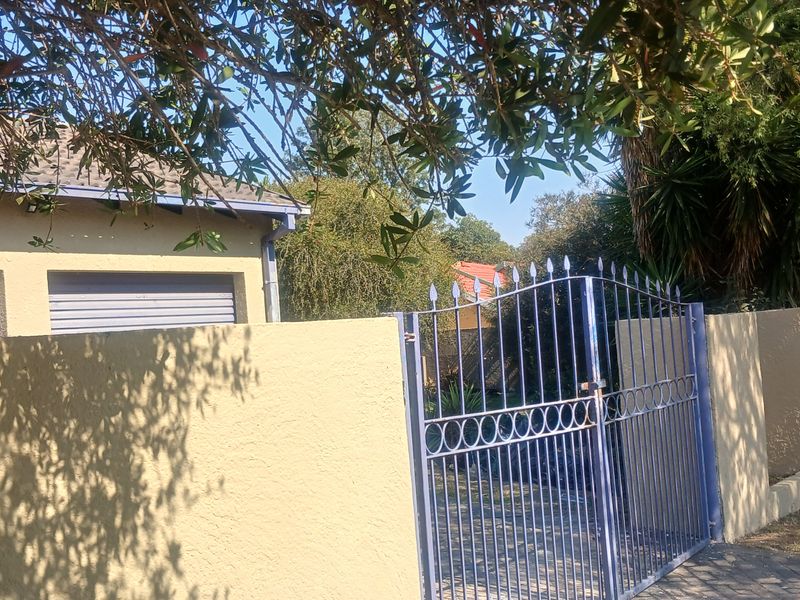 Front view of the property featuring a perimeter wall, metal entrance gate, and garage access.