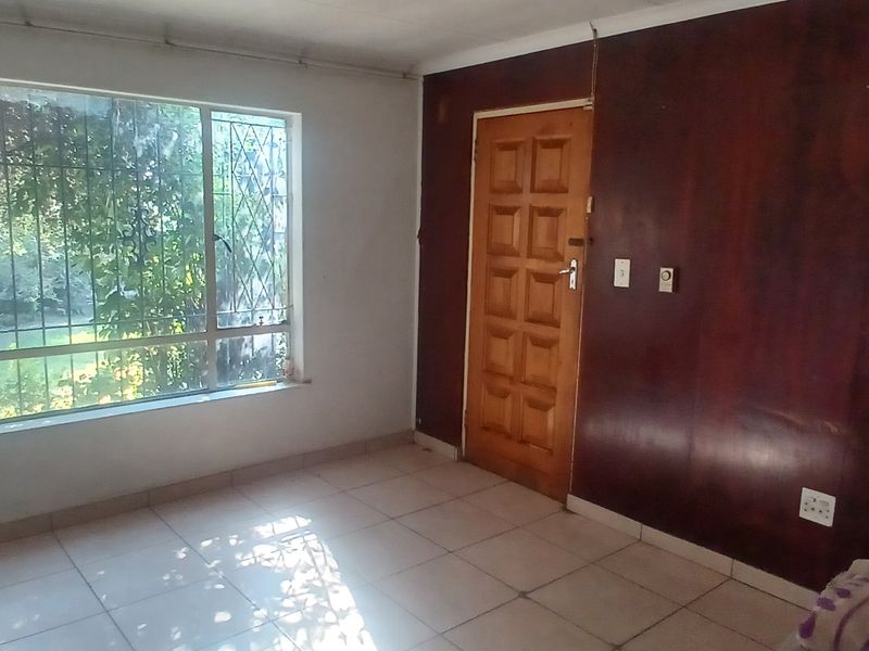 An empty living room featuring tiled flooring, a large window with security bars, and a dark timber paneled feature wall.