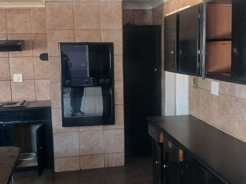 A dated kitchen featuring dark built-in cabinetry, a built-in oven, electric hob, extractor fan, and tiled splashbacks throughout.