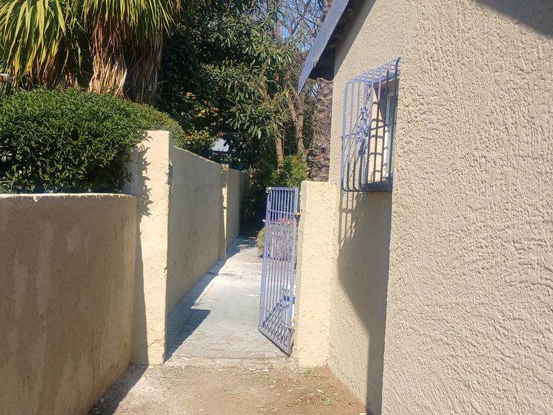 A narrow side passage featuring a paved walkway, boundary walls, and a security gate with window security bars.