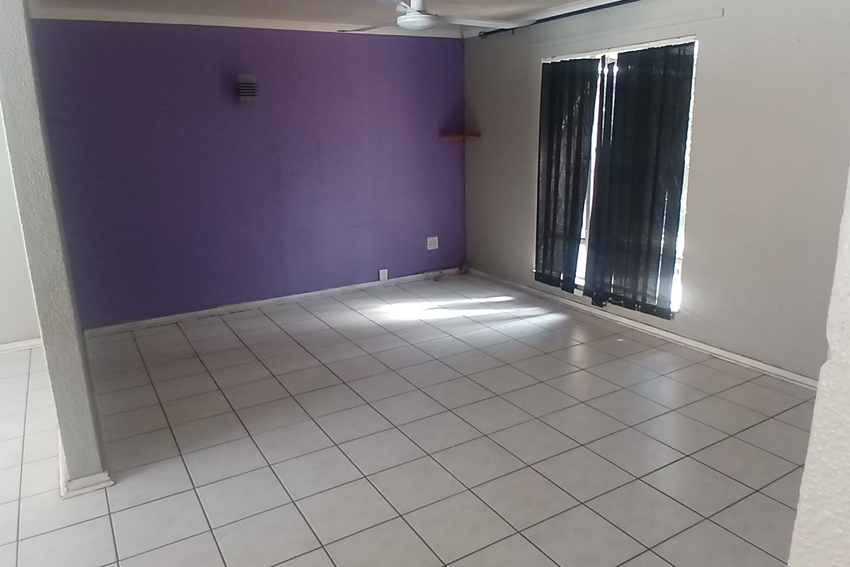 An empty living room featuring tiled flooring, a ceiling fan, and a prominent purple accent wall, offering a blank canvas for interior design.