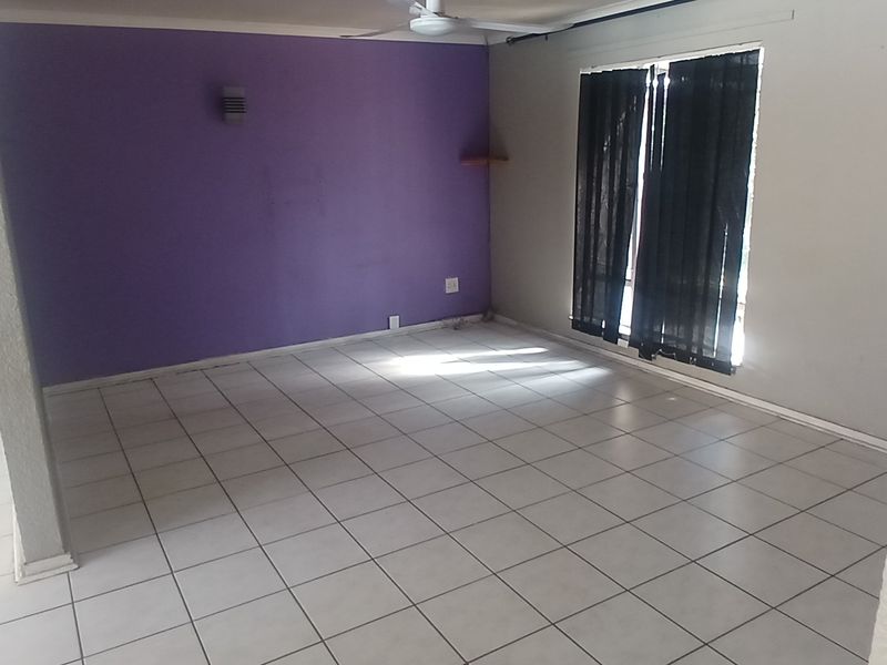 An empty living room featuring tiled flooring, a ceiling fan, and a prominent purple accent wall, offering a blank canvas for interior design.