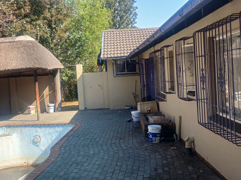 Outdoor pool area featuring a thatched lapa, brick paving, and security bars on the windows of the main dwelling.