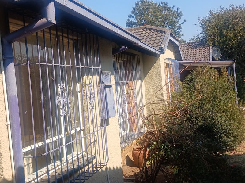 Rear exterior view of the house featuring tiled roofing, security bars on windows, and a garden area.
