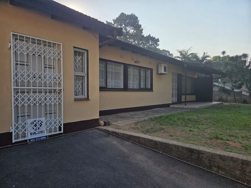 Front exterior view of the house featuring security gates, window bars, and an installed air conditioning unit with a paved walkway and lawn area.