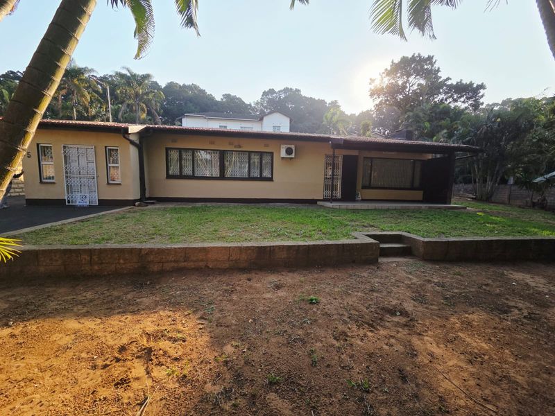 Rear view of the house featuring a tiled roof, security gates, window burglar bars, and a small lawn area with a retaining wall.