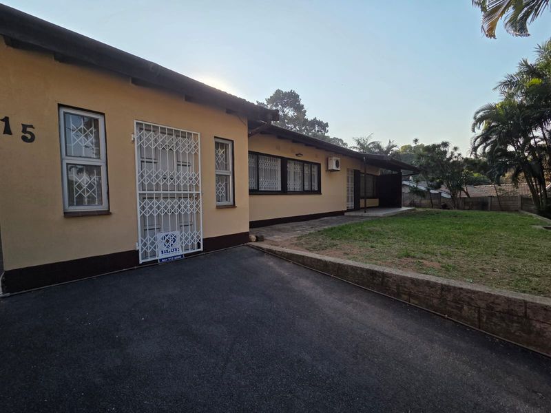 Front exterior view of the house featuring an asphalt driveway, security gates, and a small lawn area with a retaining wall.