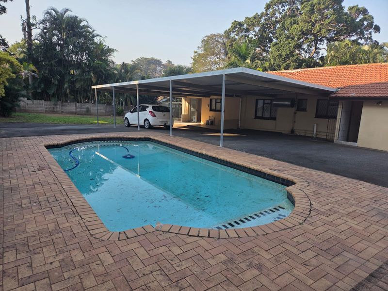 Outdoor area featuring a swimming pool with brick paving and an adjacent covered carport structure.