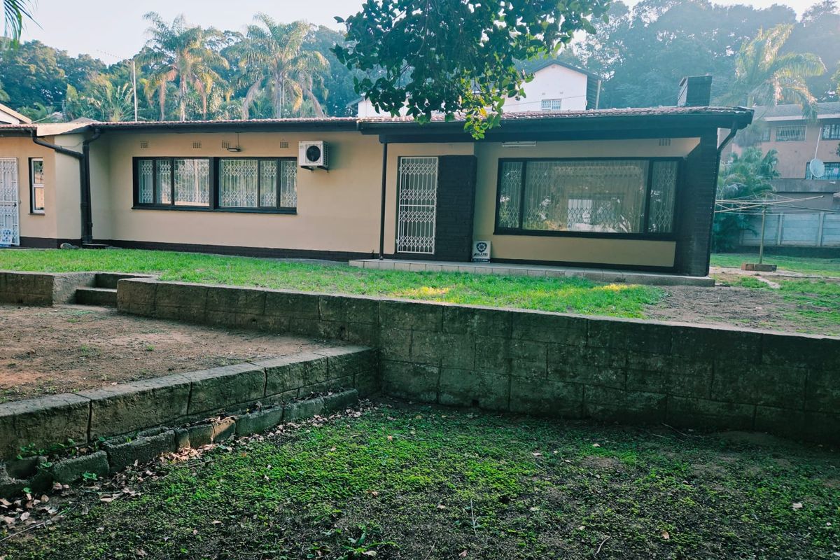 Rear view of the house featuring a retaining wall, lawn area, and exterior access with security gates and window bars.
