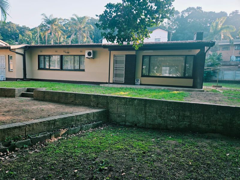 Rear view of the house featuring a retaining wall, lawn area, and exterior access with security gates and window bars.