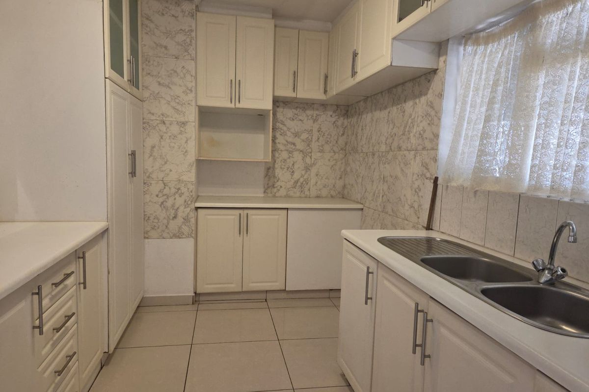 A functional kitchen featuring ample built-in cabinetry, a double bowl stainless steel sink, and tiled splashbacks, offering a clean canvas for potential modern updates.