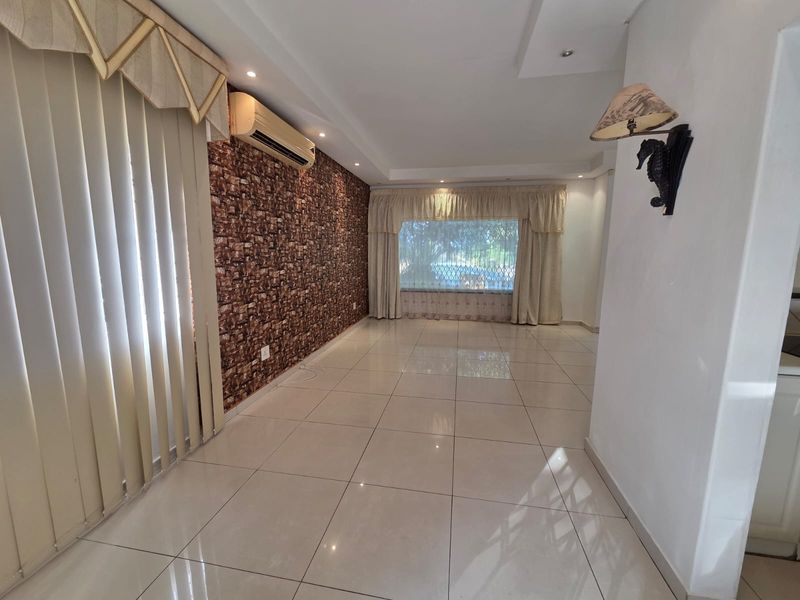 Spacious living area featuring large format floor tiles, a split-system air conditioner, and a textured feature wall, offering a bright and open layout.