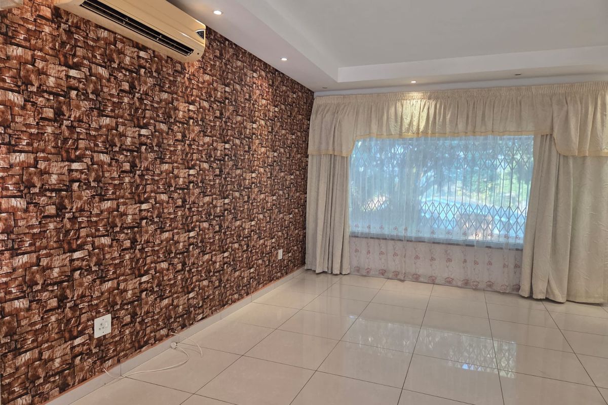 A spacious, empty living room featuring tiled floors, a textured feature wall, recessed lighting, and a wall-mounted air conditioning unit.
