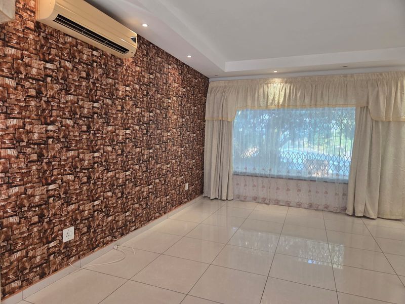 A spacious, empty living room featuring tiled floors, a textured feature wall, recessed lighting, and a wall-mounted air conditioning unit.
