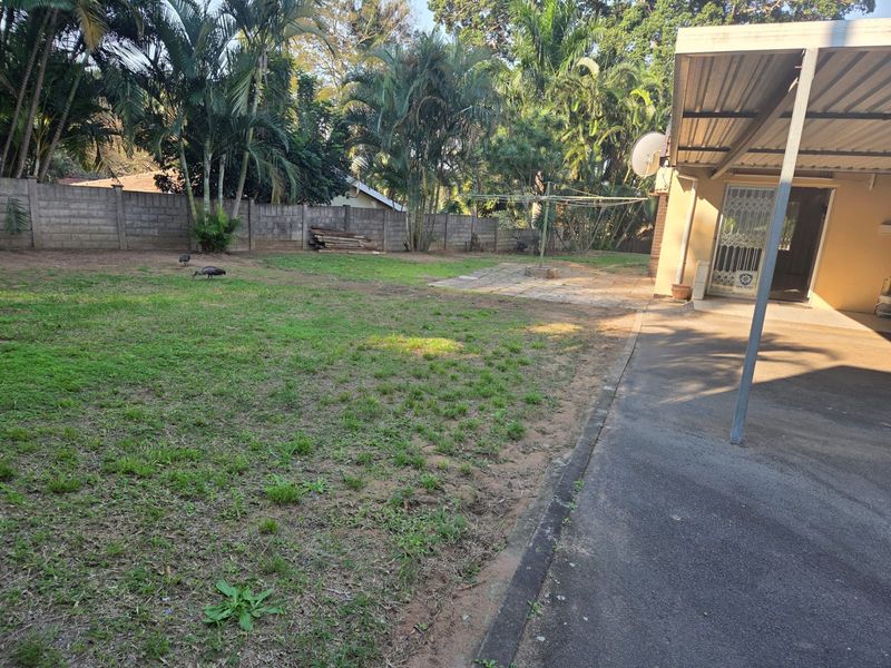 Spacious rear garden featuring a covered patio area, concrete block boundary walls, and established trees, offering potential for landscaping and outdoor living improvements.
