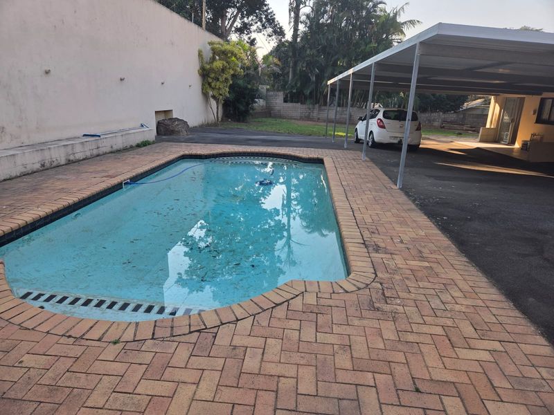 Outdoor pool area featuring a paved surround, adjacent carport structure, and boundary walling.