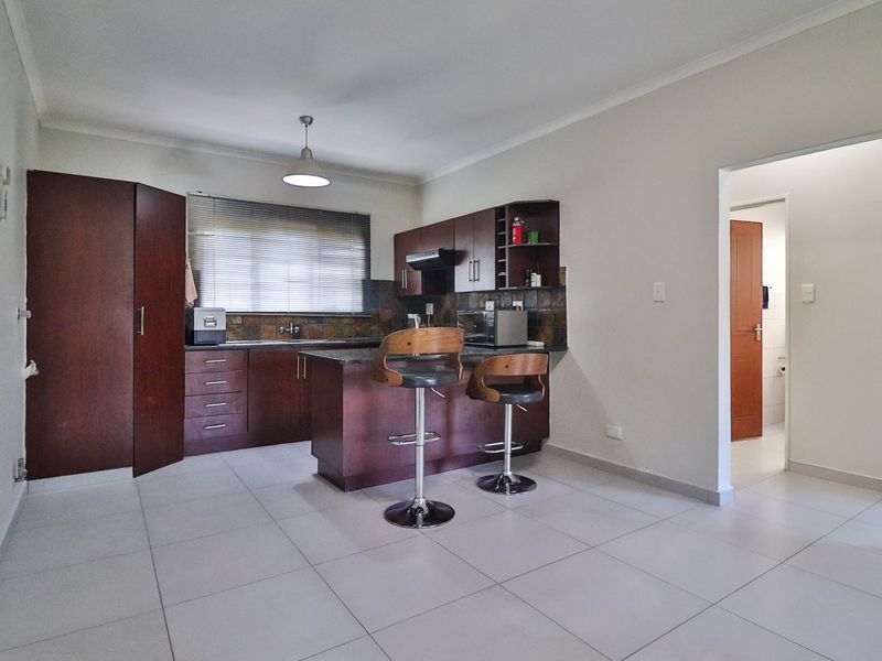A functional kitchen featuring dark wood cabinetry, stone countertops, tiled flooring, and a breakfast bar, with an adjacent doorway leading to another room.