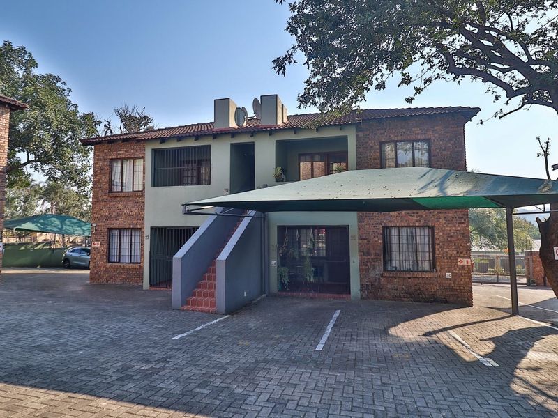 Front elevation of a two-story face-brick apartment building featuring a paved driveway, covered carport, and external staircase access.