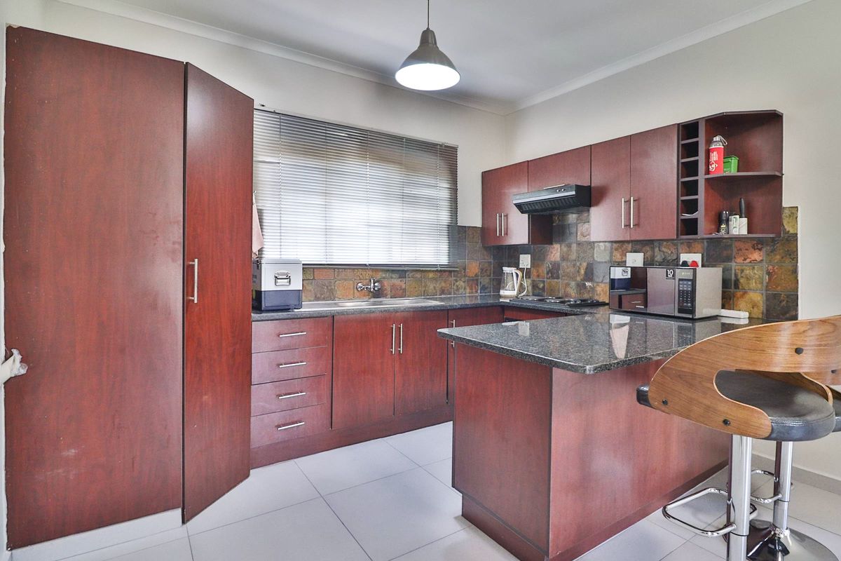 A functional kitchen featuring dark wood cabinetry, granite countertops, a slate tile backsplash, and modern ceramic floor tiles.