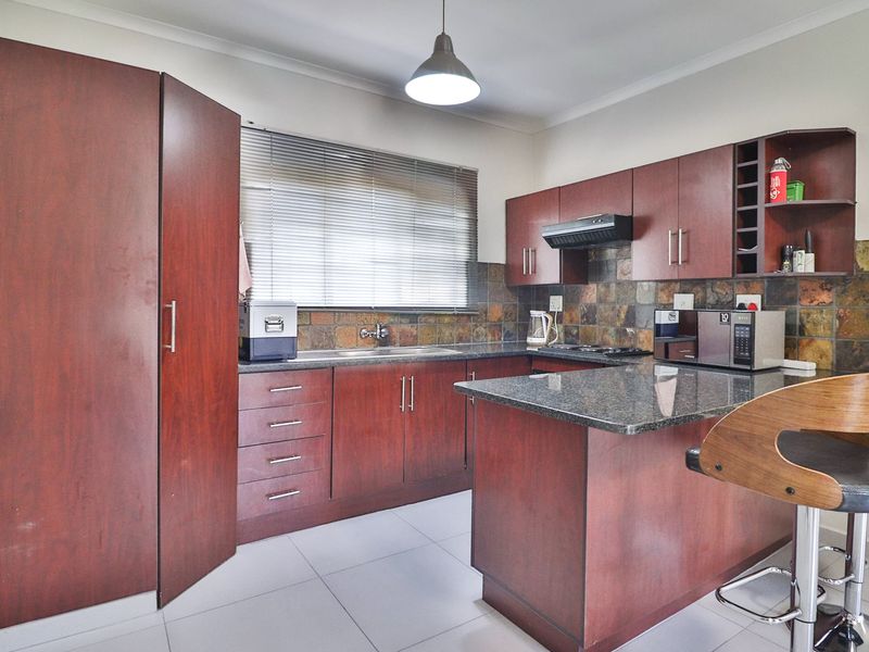 A functional kitchen featuring dark wood cabinetry, granite countertops, a slate tile backsplash, and modern ceramic floor tiles.