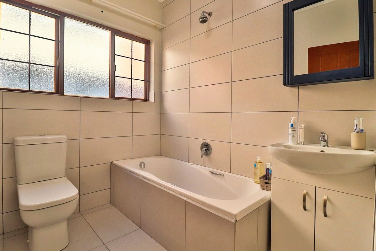 A functional bathroom featuring a built-in bathtub, wall-mounted shower, vanity cabinet with basin, and neutral tiled finishes throughout.