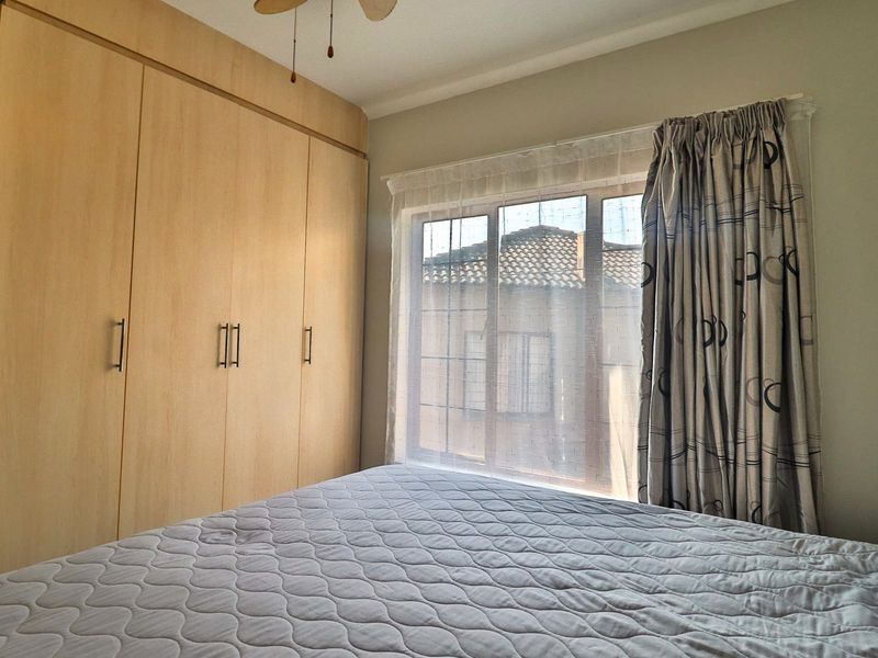 A well-maintained bedroom featuring light wood-finish built-in cupboards and a ceiling fan, offering a clean and functional living space.