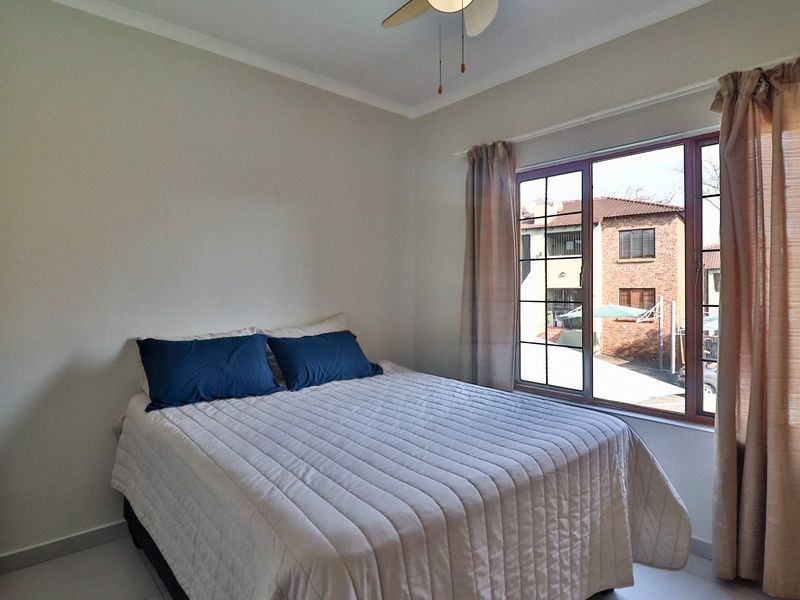 A well-lit bedroom featuring tiled flooring, a ceiling fan, and a window with security bars overlooking the exterior.