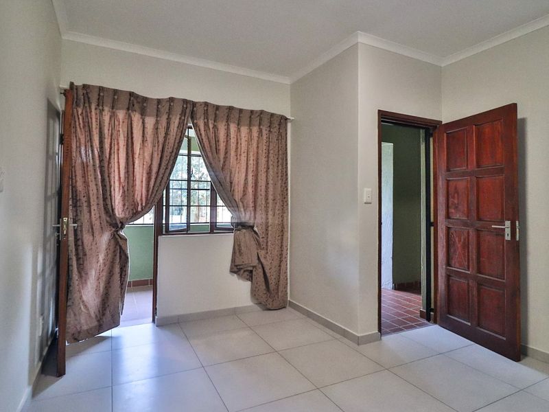 An empty bedroom featuring tiled flooring, a timber door, and access to an adjoining balcony area.