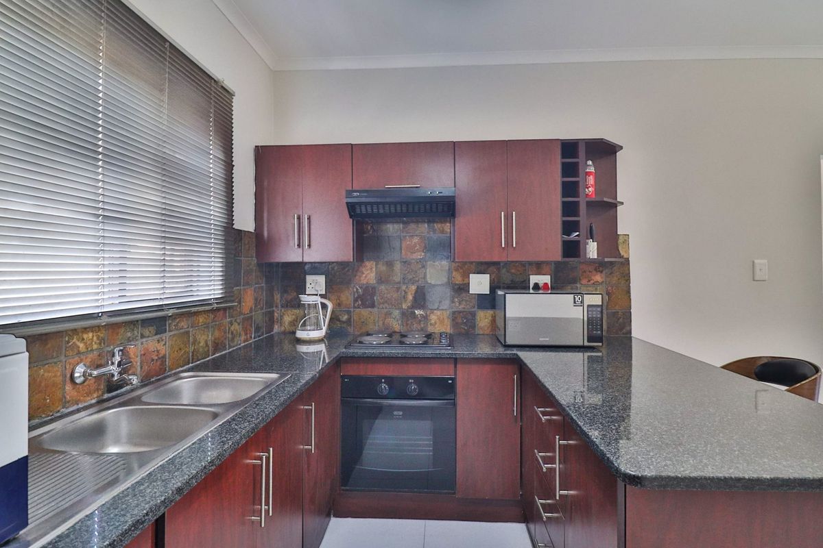 Functional kitchen featuring granite countertops, dark wood veneer cabinetry, built-in oven, electric hob, and a decorative slate tile backsplash.