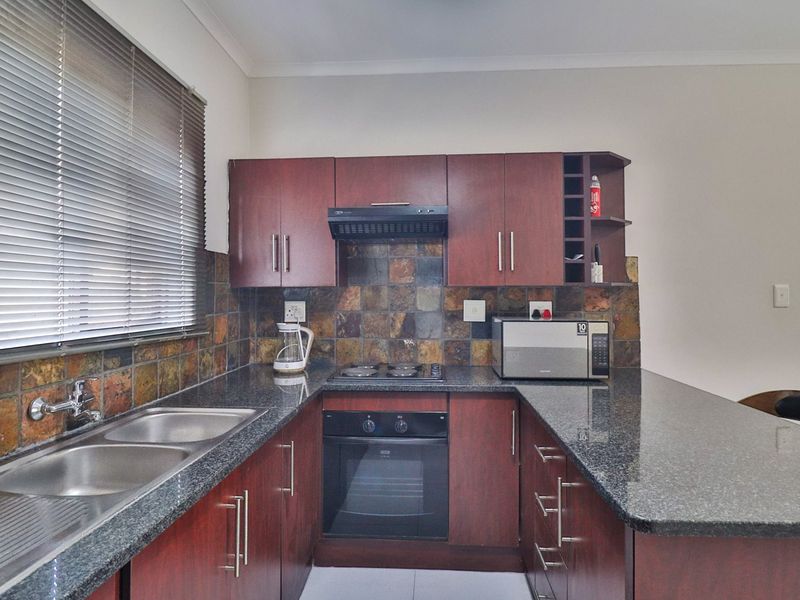 Functional kitchen featuring granite countertops, dark wood veneer cabinetry, built-in oven, electric hob, and a decorative slate tile backsplash.