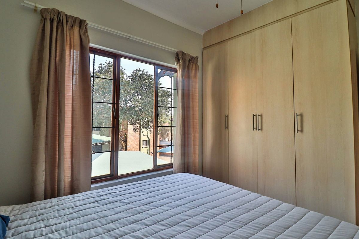 A well-lit bedroom featuring built-in wooden cupboards and a large window with views of the surrounding area.
