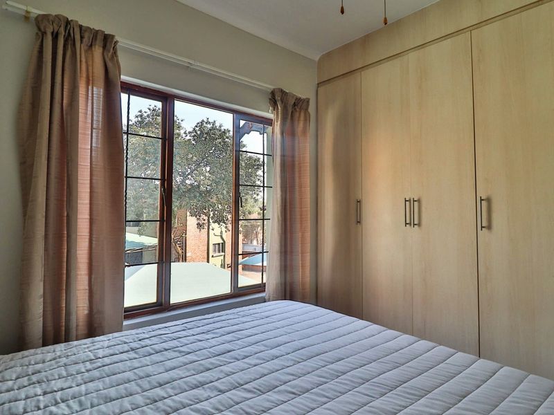 A well-lit bedroom featuring built-in wooden cupboards and a large window with views of the surrounding area.