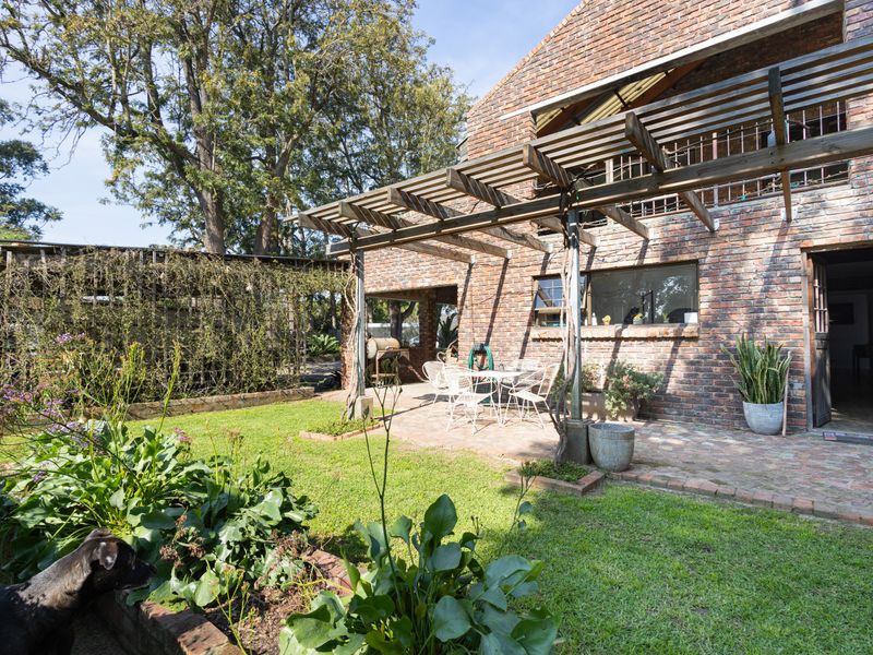 Rear exterior view featuring a classic exposed brick facade, a timber pergola over a paved patio area, and a well-established garden.