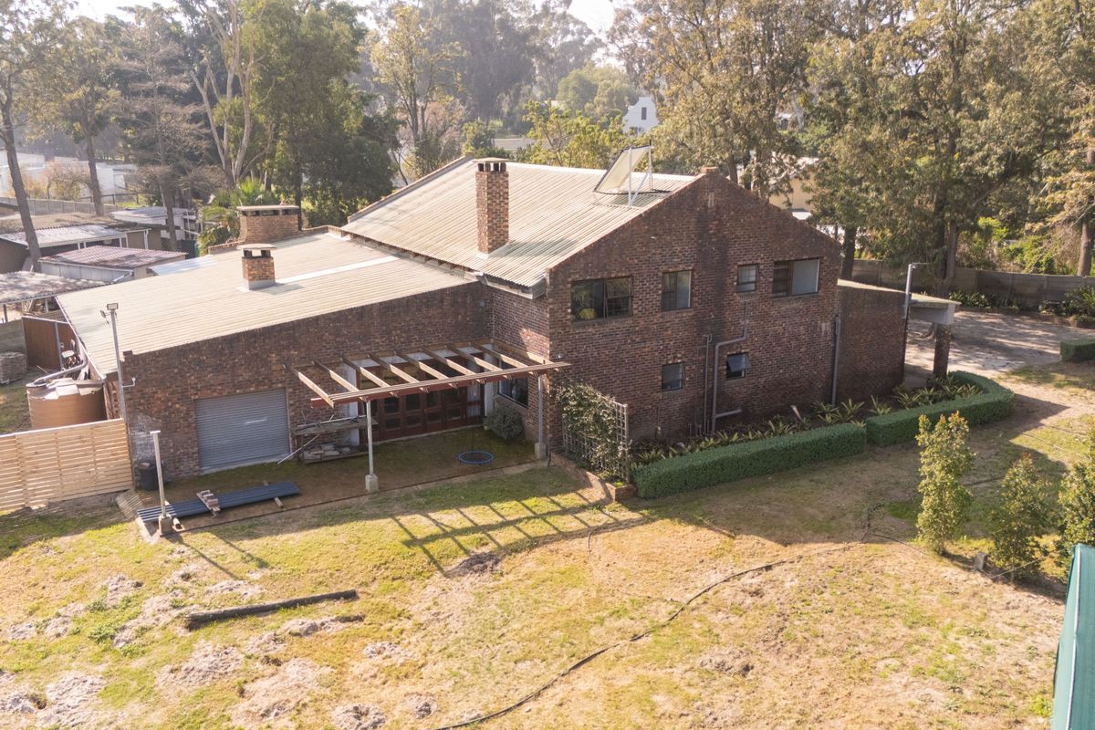 Aerial view of a multi-level brick house featuring a corrugated metal roof, solar water heating, and a timber pergola over the rear patio area.