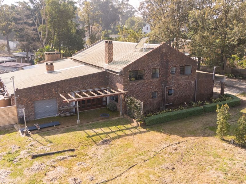 Aerial view of a multi-level brick house featuring a corrugated metal roof, solar water heating, and a timber pergola over the rear patio area.