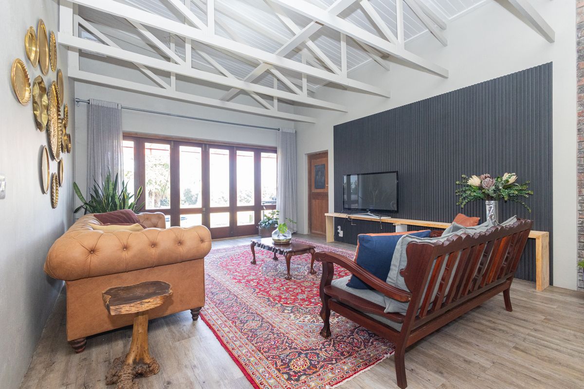 Spacious living room featuring high vaulted ceilings with exposed white trusses, a modern vertical slat feature wall, and large timber-framed folding doors.