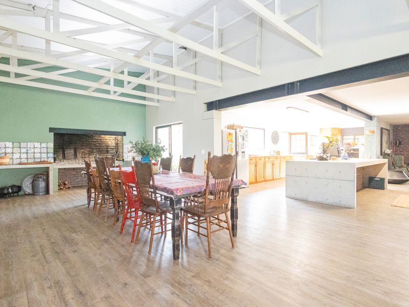 Spacious open-plan living and dining area featuring exposed roof trusses, a built-in fireplace, and a modern concrete kitchen island.