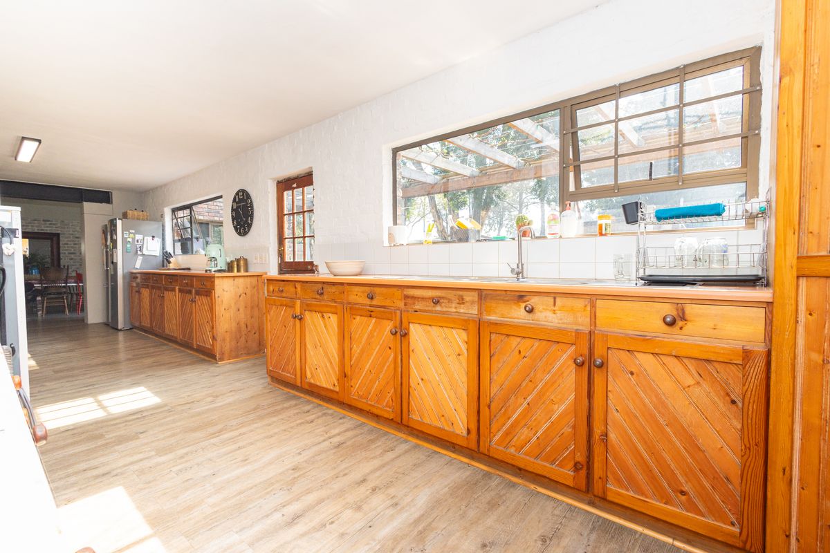 Spacious kitchen featuring extensive wooden cabinetry, a stainless steel sink, tiled backsplash, and durable laminate flooring with natural light.